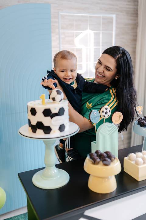 no colo da mamãe diante da mesa do bolo durante sua festa de 1 ano.'