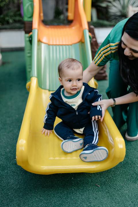 Bebê brincando no escorregador durante a comemoração do seu primeiro aniversário.'