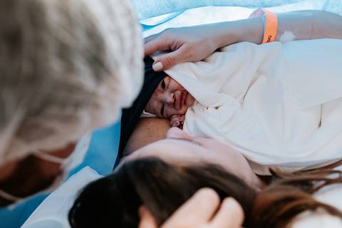 Primeiro abraço em família com o bebê recém-nascido no peito da mãe.'