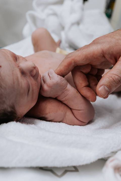 Mão segurando a mãozinha do bebê recém-nascido.'