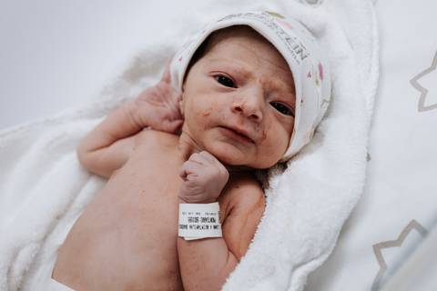 Bebê recém-nascido enrolado na manta olhando para a câmera.'