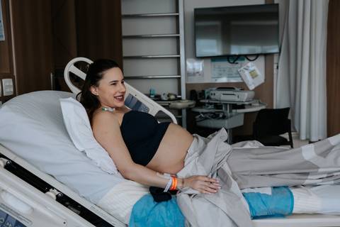 Gestante reclinada na cama hospitalar sorrindo.'