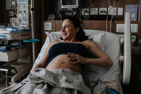 Gestante sorrindo descontraída na cama do hospital.'