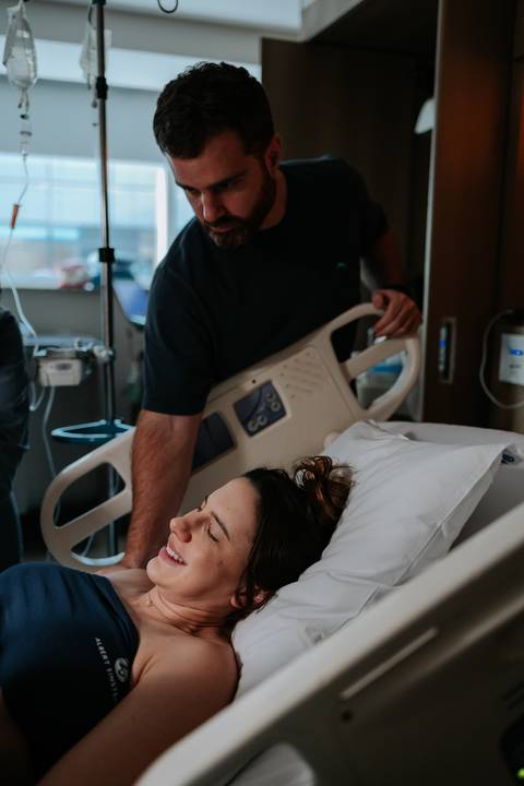 Acompanhante inclinado apoiando a gestante deitada na cama.'