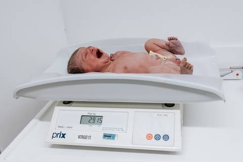 Bebê sendo pesado na balança pediátrica da maternidade.'