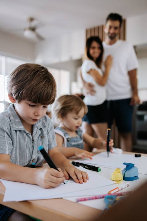 Crianças desenhando com canetinhas na mesa de atividades.'
