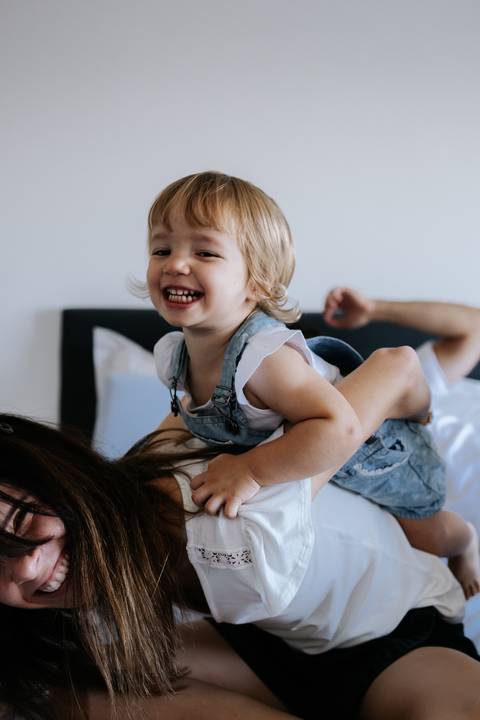 Menina dando risada em cima das costas da mãe.'