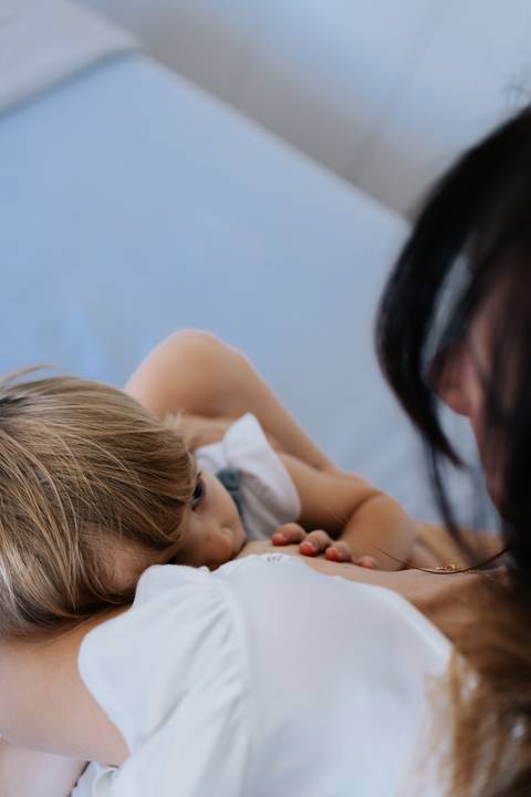 Mãe e filha deitadas juntinhas descansando na cama.'