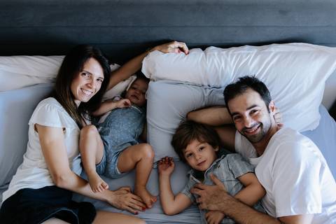 Vista superior da família toda deitada na cama sorrindo.'