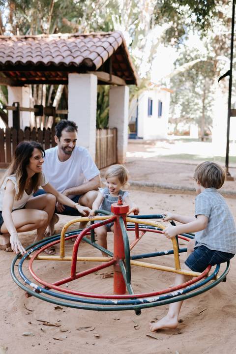Família reunida brincando no carrossel do parquinho.'