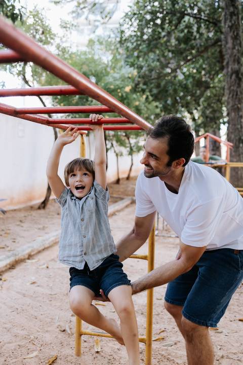 Menino se pendurando no trepa-trepa com ajuda do pai.'