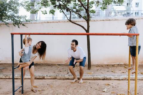 Pais brincando com os filhos na área do parquinho de areia.'
