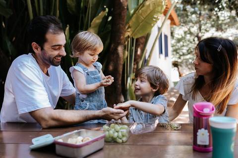 Família reunida fazendo lanche na mesa ao ar livre.'