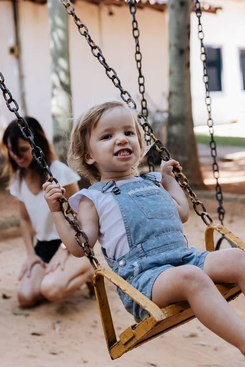 Menina de jardineira se balançando no balanço do parque.'