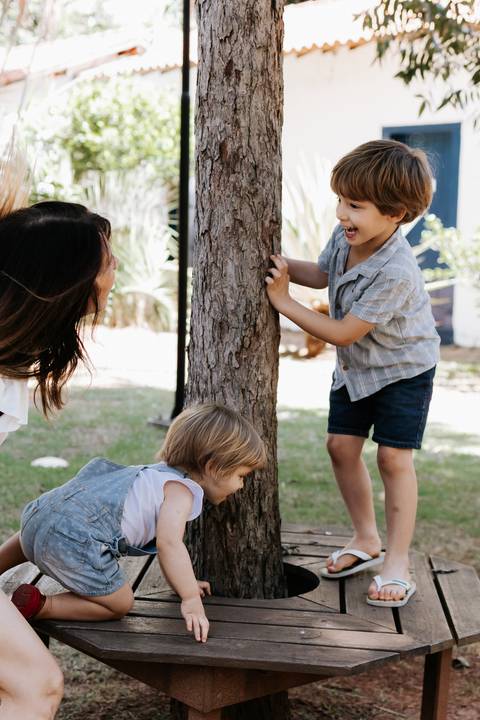 Mãe e filhos brincando de esconde-esconde atrás da árvore.'