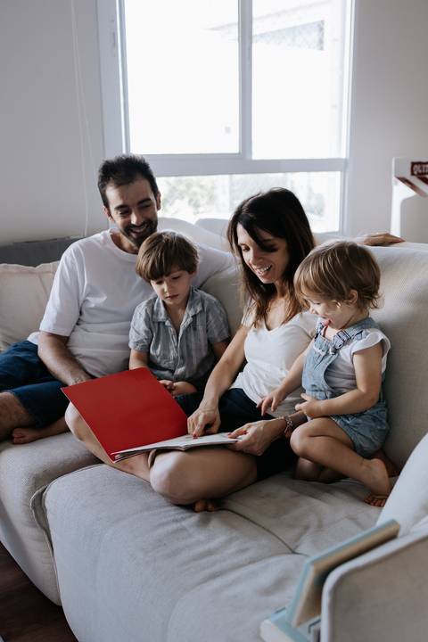 Família reunida no sofá folheando um livro juntos.'