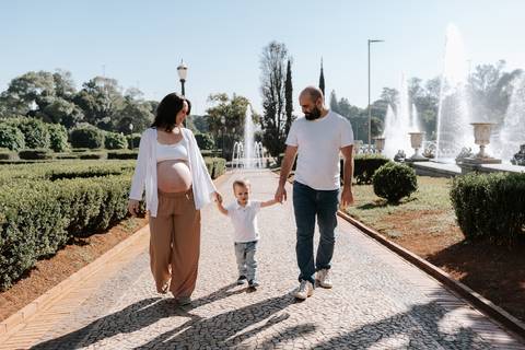 Casal caminhando de mãos dadas com o filho em alameda com fontes ao fundo.'