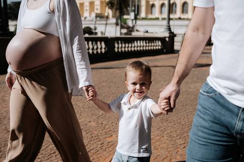 Menino sorridente caminhando de mãos dadas entre os pais, com selo 