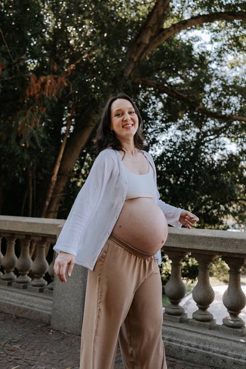 Gestante caminhando ao ar livre sorrindo e exibindo a barriga.'