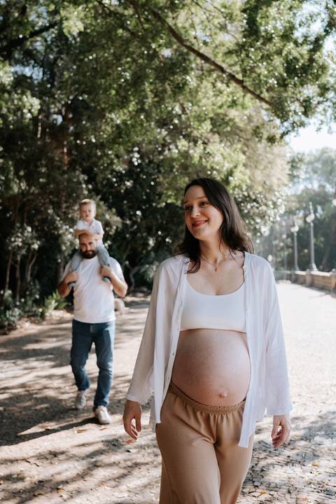 Gestante em primeiro plano com o pai e o filho no fundo.'