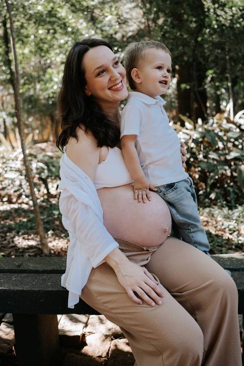 Menino sentado no colo da mãe com a mão na barriga gestante.'