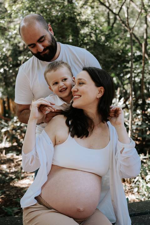 Menino nas costas da mãe gestante sorrindo juntos ao ar livre.'