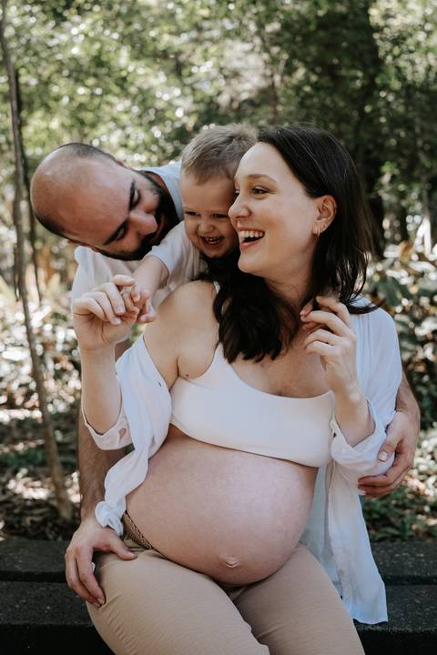 Casal sorridente e o filho reunidos em abraço na natureza.'