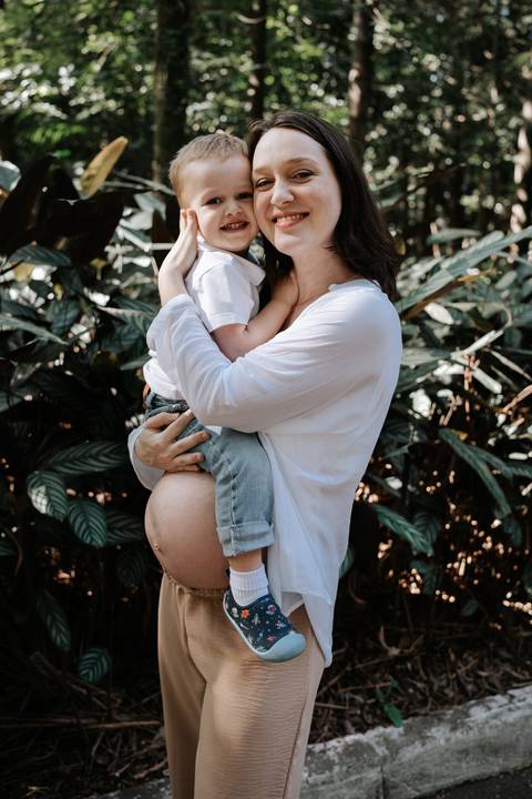 Mãe gestante segurando o filho no colo em meio às plantas.'