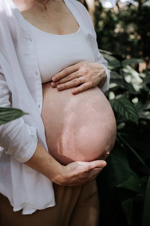 Close-up da barriga de gestante com as mãos apoiadas delicadamente.'