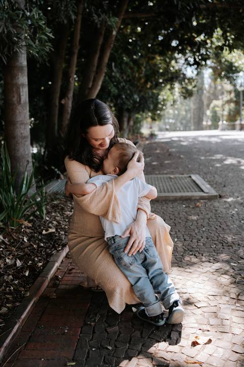 Mãe e filho abraçados carinhosamente sentados no parque.'