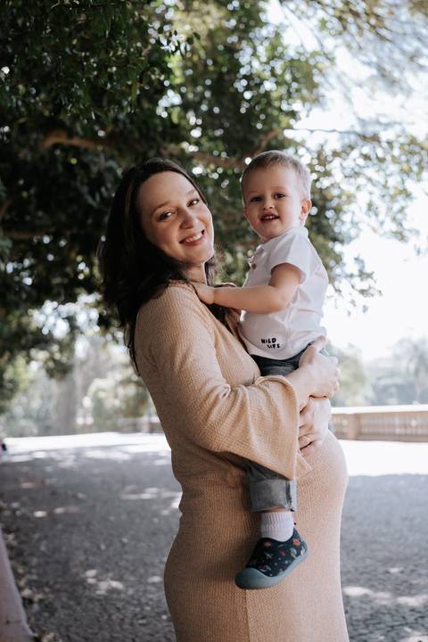 Mãe sorridente com o filho no colo perto da balaustrada.'