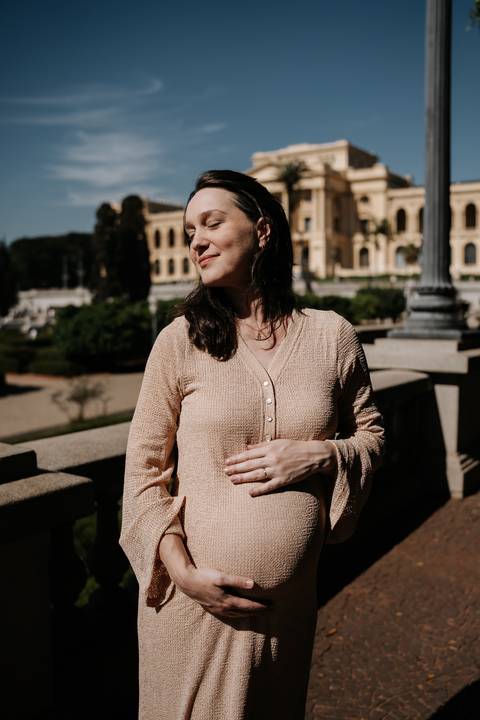 Gestante posando ao sol com o museu ao fundo.'