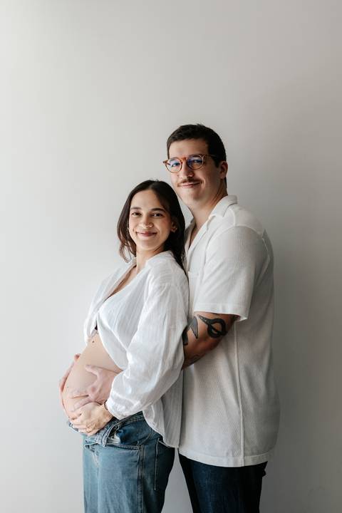Casal abraçado sorrindo para a câmera em fundo neutro.'