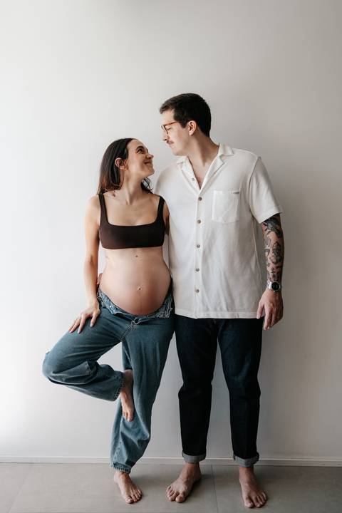 Casal em pé lado a lado exibindo a barriga de gravidez.'