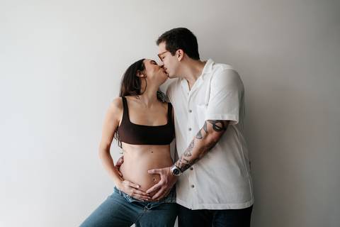 Pai beijando a gestante enquanto segura a barriga.'