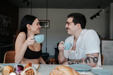 Casal tomando café da manhã e conversando na mesa.'