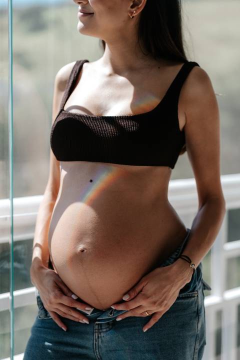 Close da barriga da gestante com feixe de luz do arco-íris.'