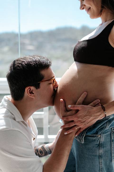 Close do pai beijando carinhosamente a barriga da gestante.'