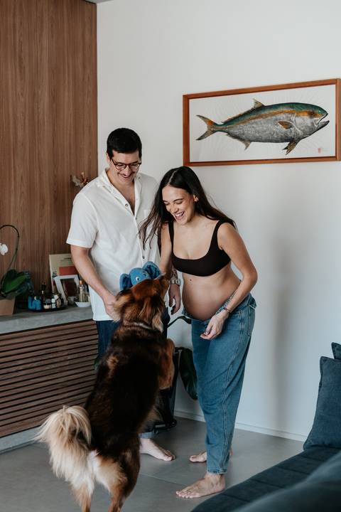 Casal e o cachorro sorrindo juntos no ambiente da sala.'