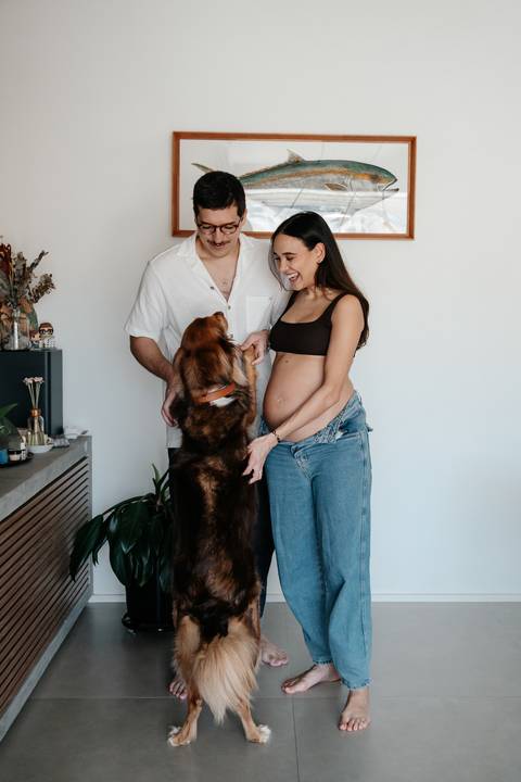 Casal e o cachorro em pé posando juntos na sala.'