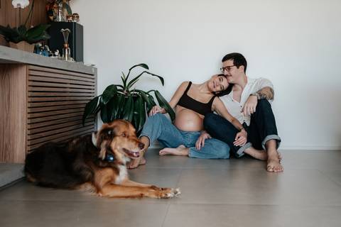 Casal sentado no chão ao fundo com o cachorro deitado em primeiro plano.'