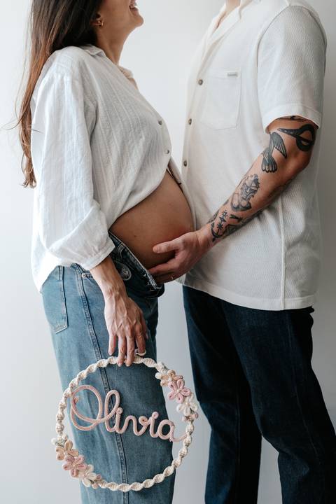 Detalhe das mãos do pai acariciando a barriga da gestante.'
