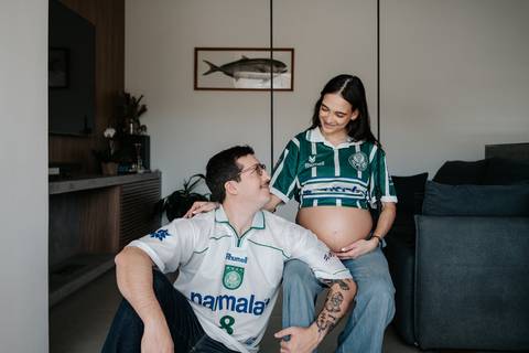 Casal vestindo camisas retro do Palmeiras sorrindo no sofá.'