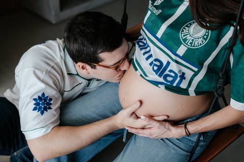 Pai beijando a barriga da gestante usando camisa do Palmeiras.'