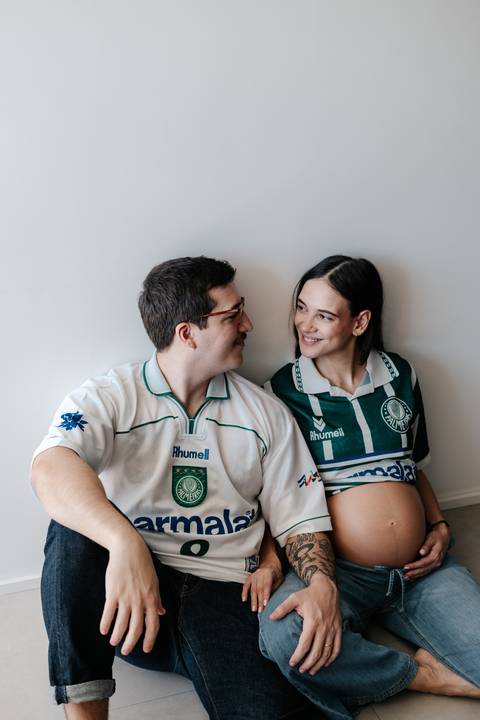 Casal sentado no chão trocando olhares com camisas de time.'
