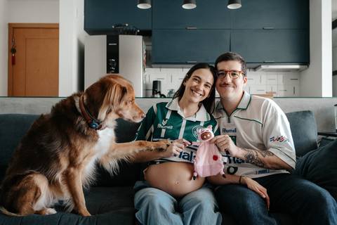 Casal no sofá com o cachorro colocando a pata na barriga.'