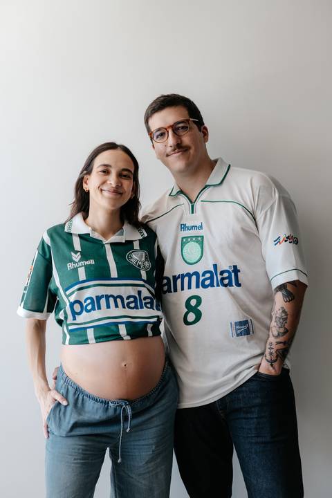 Retrato do casal sorridente em pé vestindo camisas do Palmeiras.'