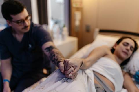 Casal de mãos dadas durante contração no quarto hospitalar.'
