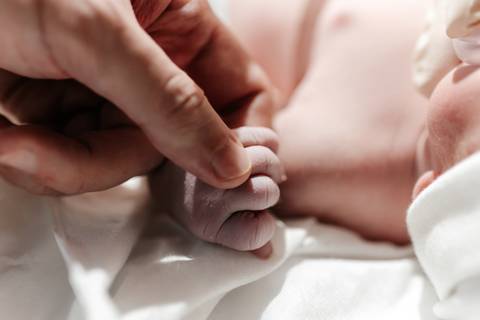 Mão do pai tocando com delicadeza a mãozinha do bebê.'