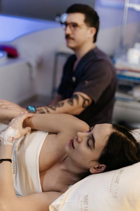 Acompanhante acariciando o ombro da gestante deitada na cama.'